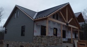 front part of home with new metal roof, post and beam custom home, under construction, Timberhaven, log homes, log cabins, log cabin kits, contemporary siding, black standing seam metal, stone accents on home, laminated, kiln dried, custom post and beam home