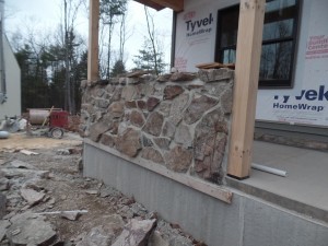 side of porch with solid wall with real mountain stone, post and beam custom home, under construction, Timberhaven, log homes, log cabins, log cabin kits, contemporary siding, black standing seam metal, stone accents on home, laminated, kiln dried, custom post and beam home