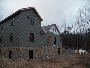 rear of home with mountain stone and siding application, post and beam custom home, under construction, Timberhaven, log homes, log cabins, log cabin kits, contemporary siding, black standing seam metal, stone accents on home, laminated, kiln dried, custom post and beam home