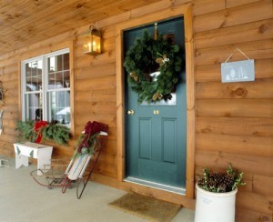 front porch of log home decorated for Christmas, Timberhaven log homes, log homes, log cabin kits, log cabins, Merry Christmas, stone fireplace, fireplace in dining room, natural light, white pine