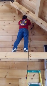 log home owner standing on beam sanding log wall, Timberhaven Log Homes, log homes, log cabin homes, log cabins, post and beam homes, timberframe homes, timber frame homes, laminated logs, engineered logs, floor plan designs, kiln dried logs, Timberhaven local reps, log home builders, interior wall coverings, log homes in PA